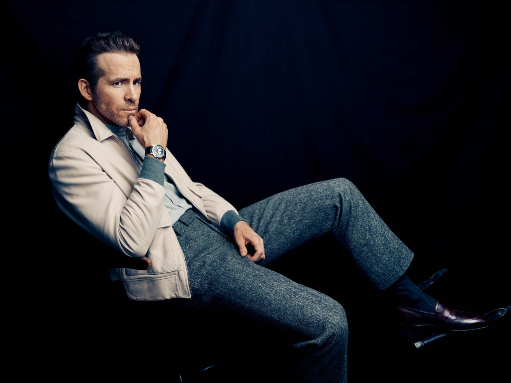 Actor Ryan Reynolds is sitting on a chair with a clock on his hand