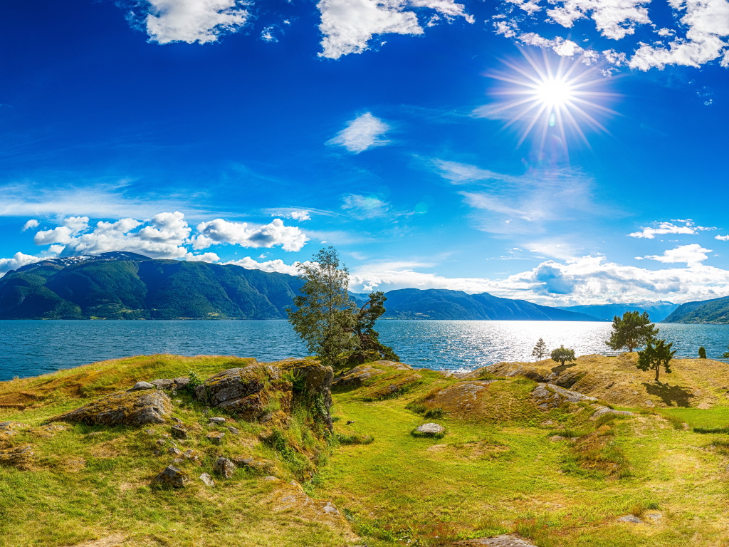 Красивое яркое солнце в голубом небе над горами и водой, Исландия
