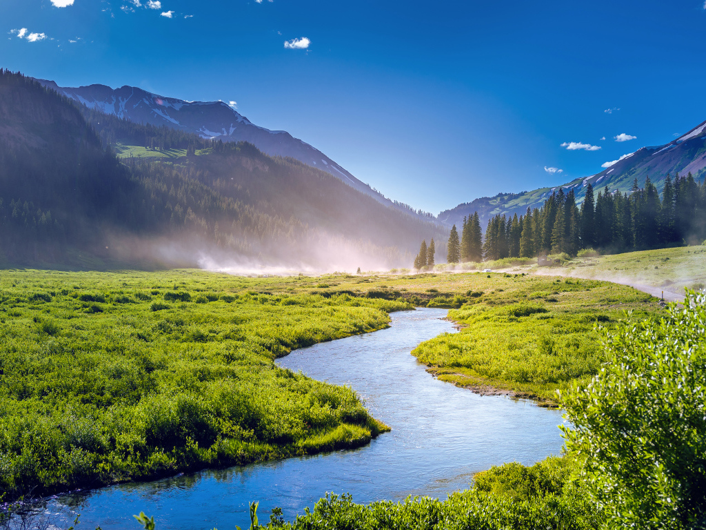 Речка на фоне покрытых зеленью гор под голубым небом