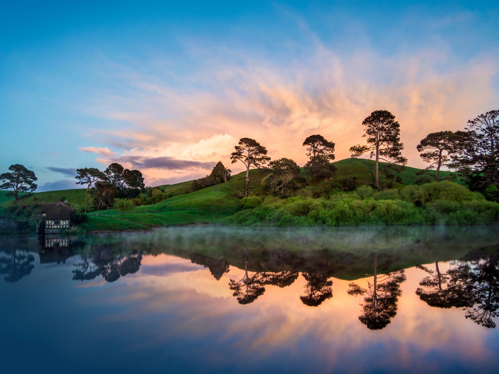 Деревья отражаются в воде на берегу озера на закате