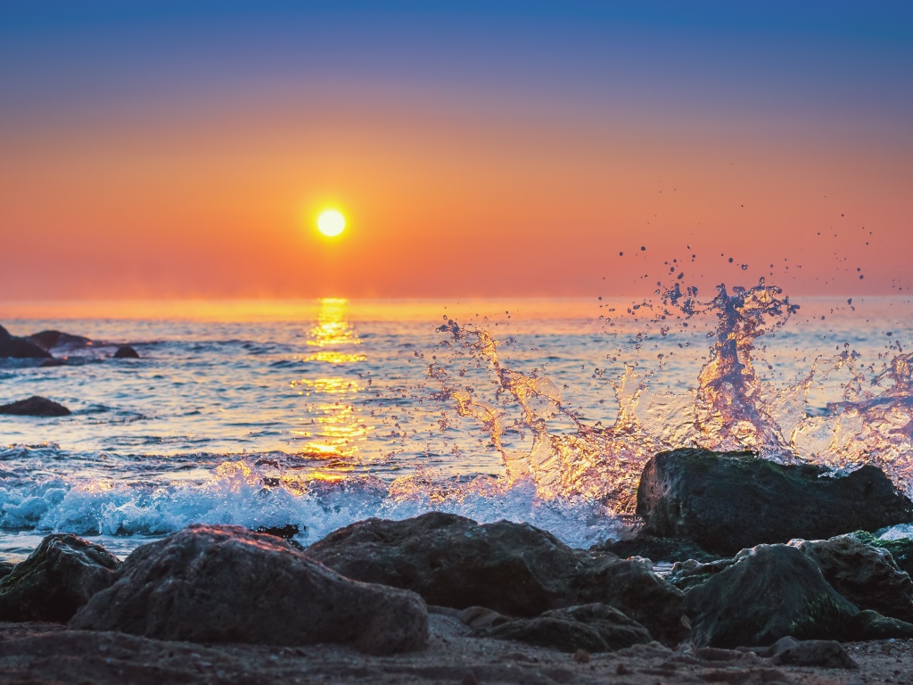 Волны бьются о камни на морском побережье на закате