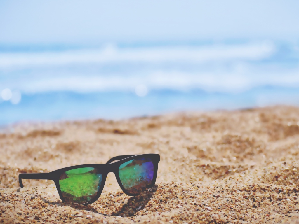 Солнцезащитные очки лежат на желтом песке у моря