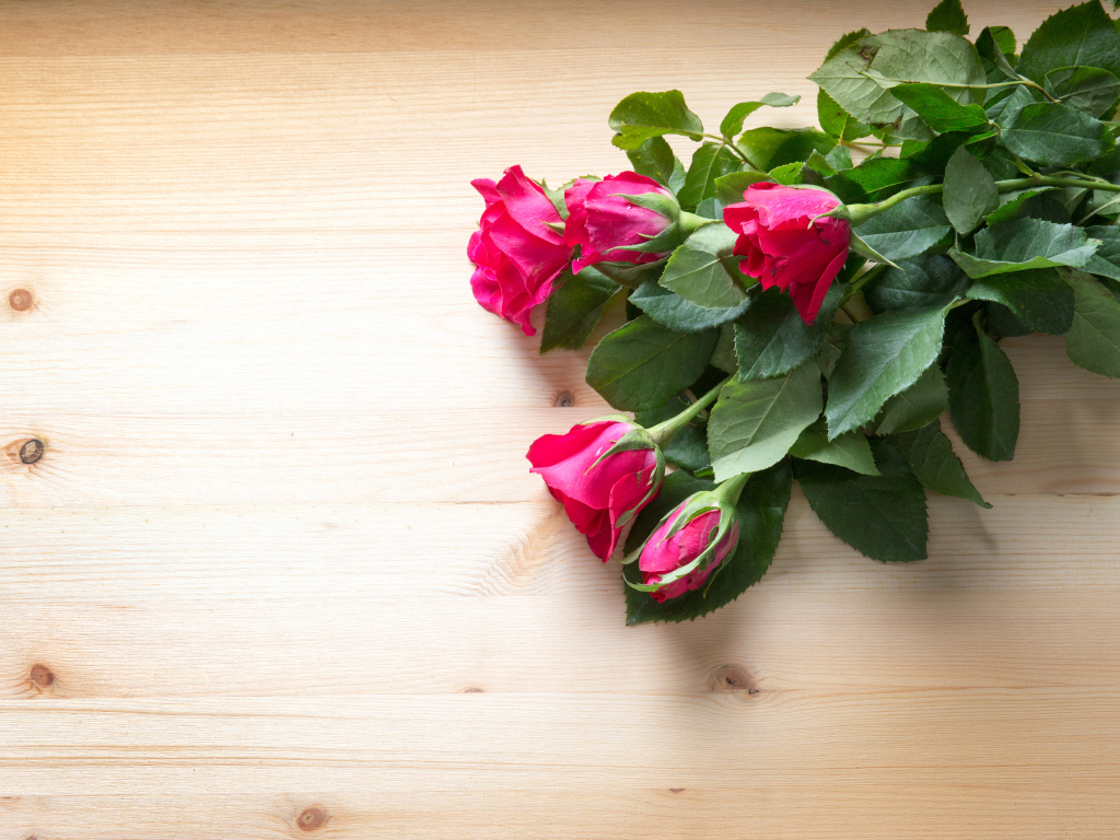 Букет розовых роз с зелеными листьями на деревянной поверхности 