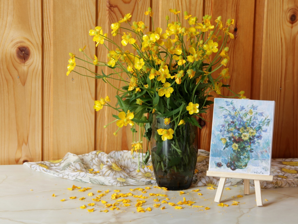 Букет желтых полевых лютиков в стеклянной вазе на столе с картиной