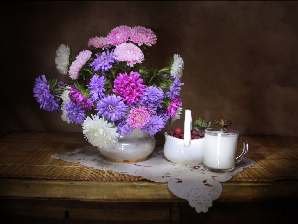 Букет разноцветных астр в вазе на столе с молоком и ягодами малины