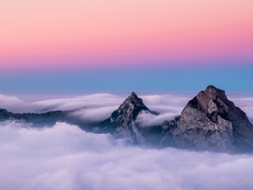 Верхушки гор в белых облаках под красивым розовым небом 