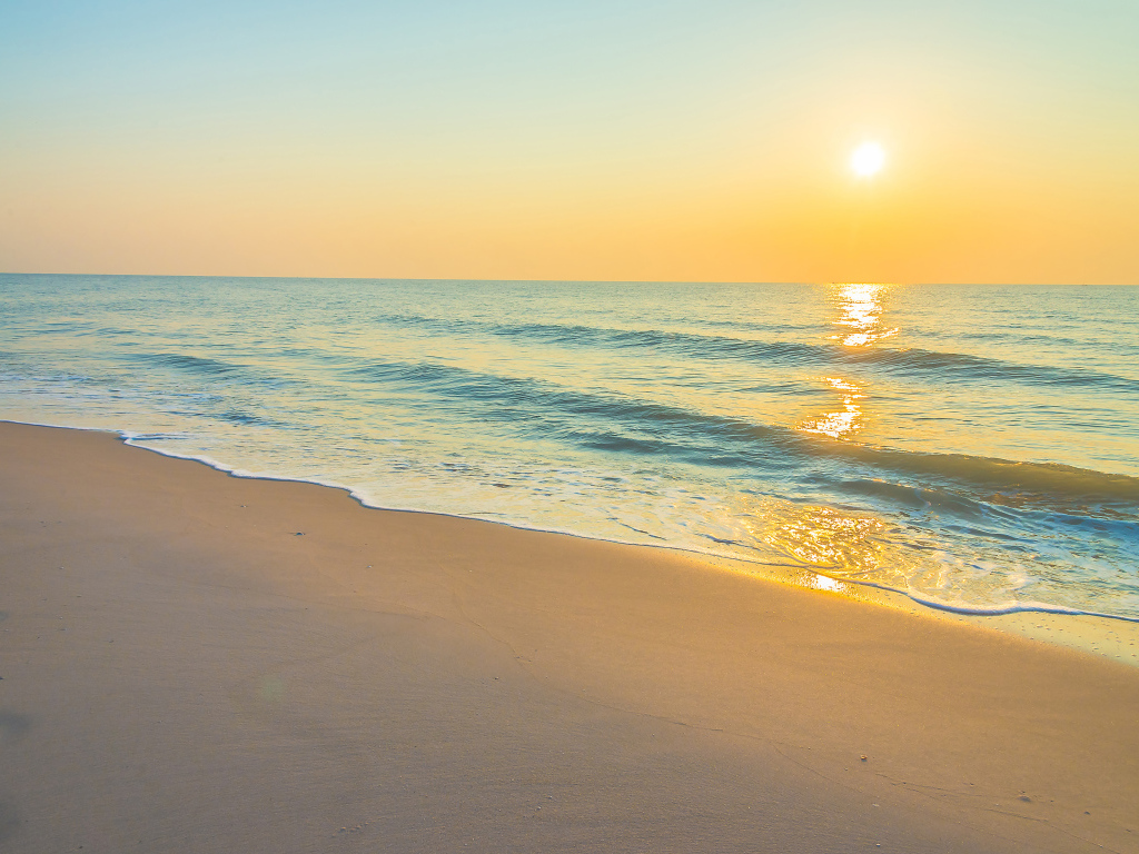 Морские волны на желтом песке на закате солнца летом