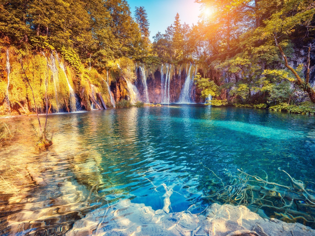 Водопад в лучах солнца стекает со скалы в реку