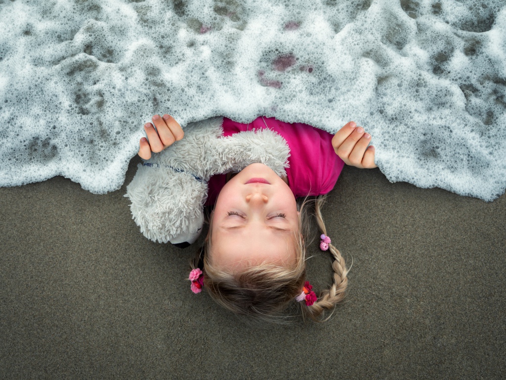Маленькая девочка спит на песке под одеялом из морской пены