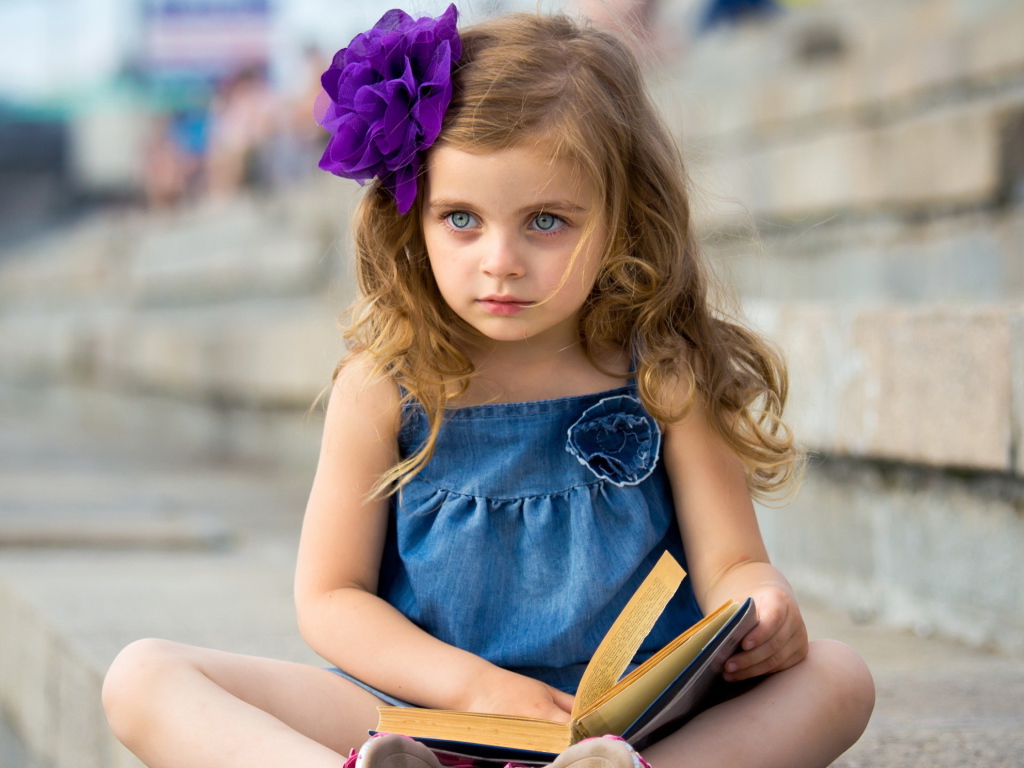 Маленькая девочка с цветком в волосах сидит на ступенях