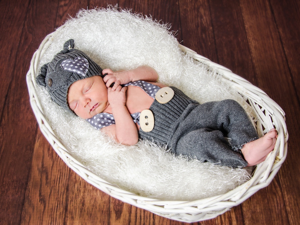 Спящий младенец в сером костюме в белой корзине