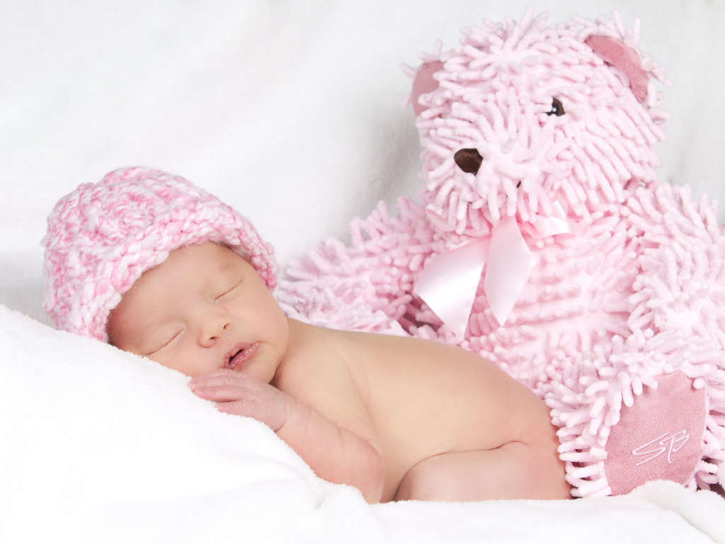 Спящий грудной ребенок в шапке с большим розовым медведем