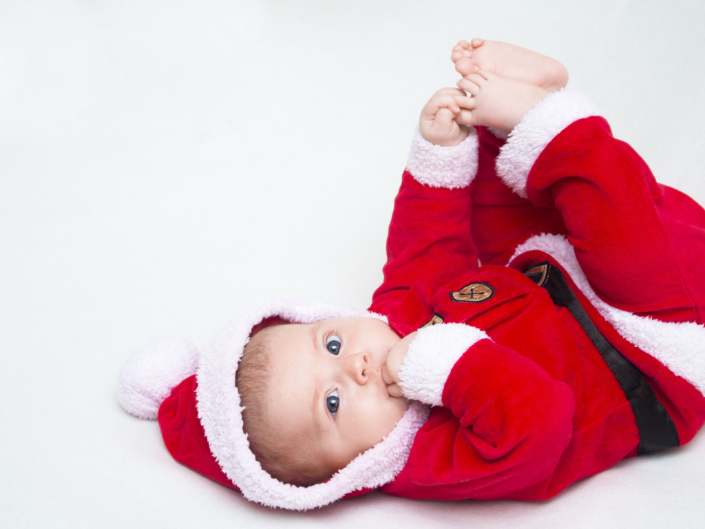 Маленький ребенок в красном новогоднем костюме на сером фоне