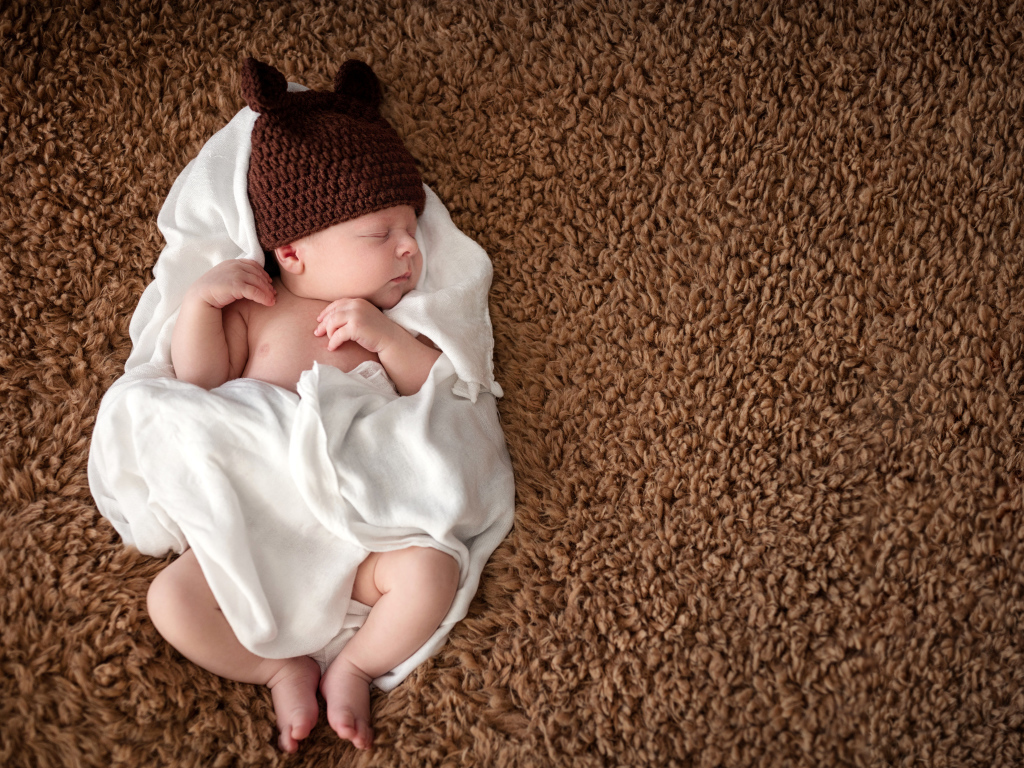 Младенец в коричневой вязаной шапке в белом покрывале 