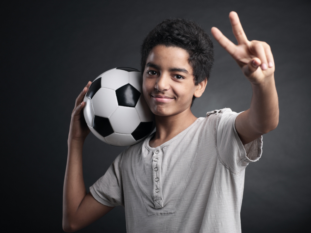 Мальчик с футбольным мячом на плече на сером фоне