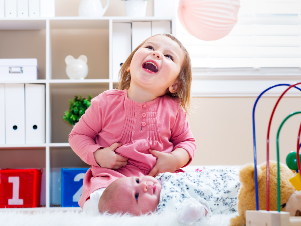 Смеющаяся маленькая девочка с младенцем