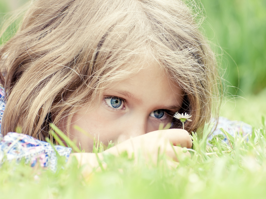 Маленькая голубоглазая девочка на траве с ромашкой