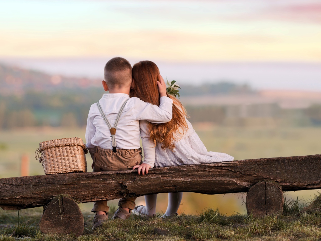 Маленькие мальчик и девочка обнимают друг друга на лавке