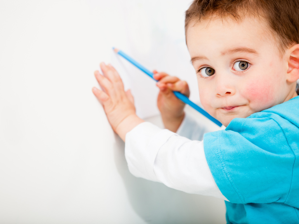 Маленький мальчик рисует карандашом на стене