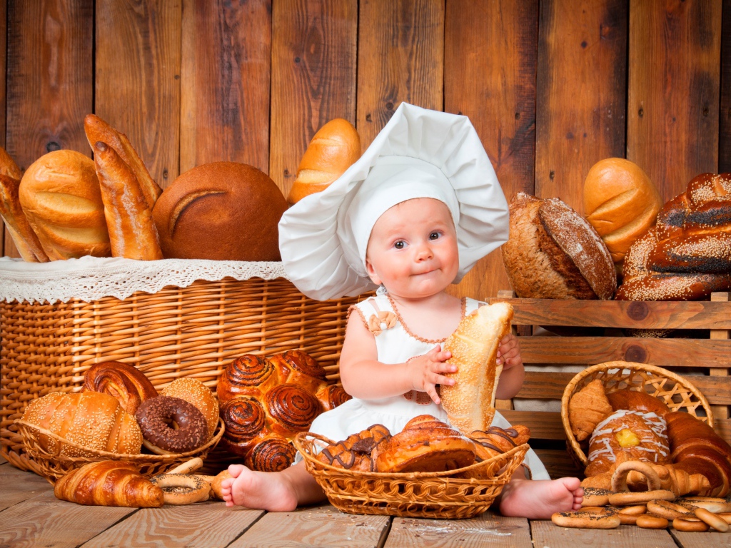 Маленький мальчик в костюме повара сидит на столе с выпечкой