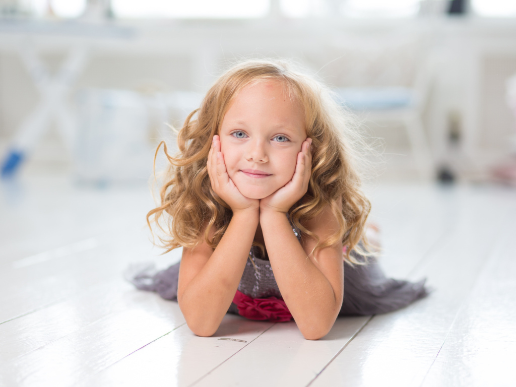 Маленькая длинноволосая голубоглазая девочка лежит на полу