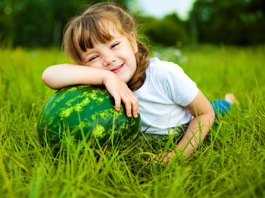 Улыбающаяся девочка с зеленым арбузом на траве