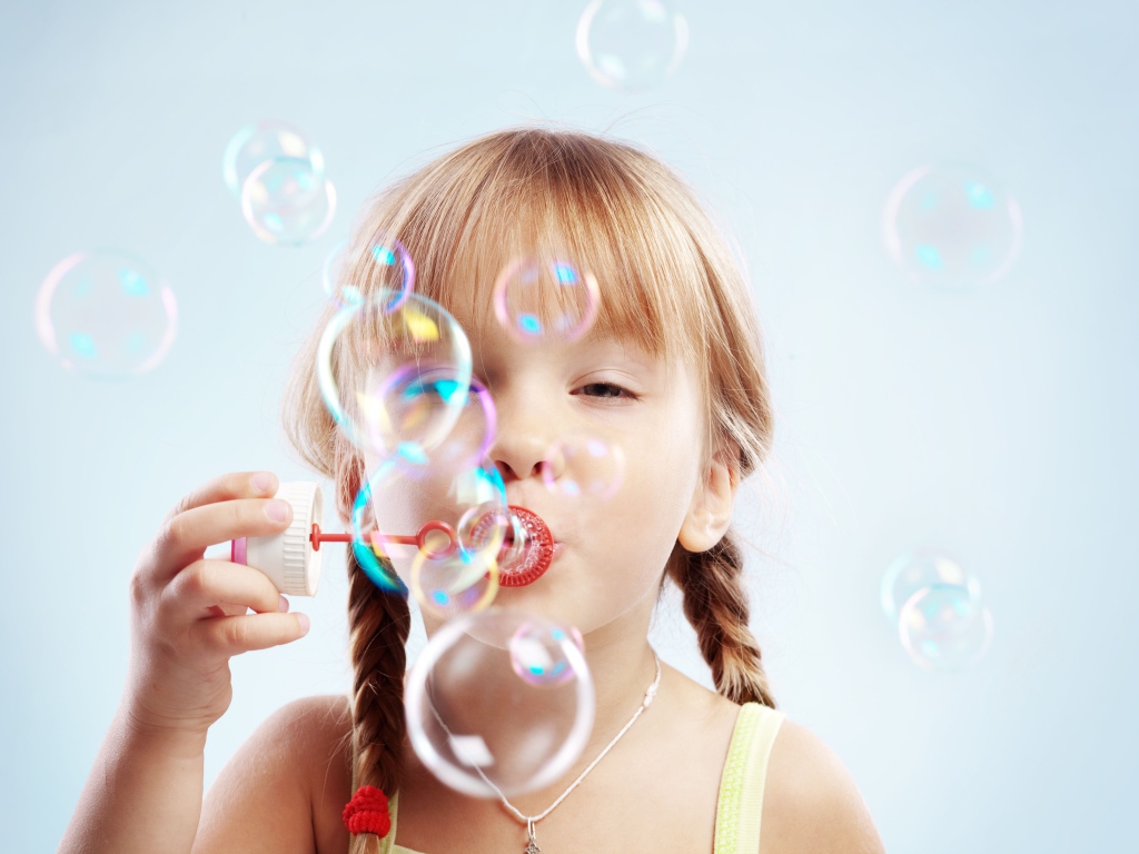 Девочка с косичками пускает мыльные пузыри