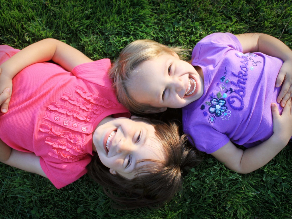 Две маленьких улыбающихся девочки лежат на зеленой траве