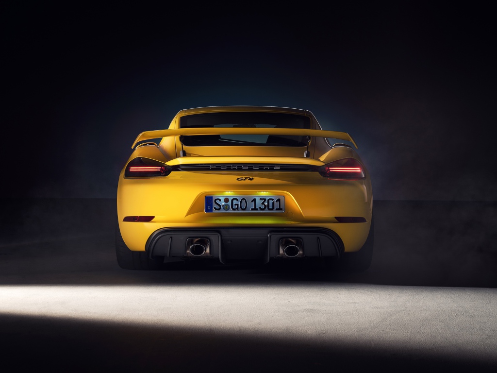 Желтый автомобиль Porsche 718 Cayman GT4, 2019 года вид сзади на сером фоне