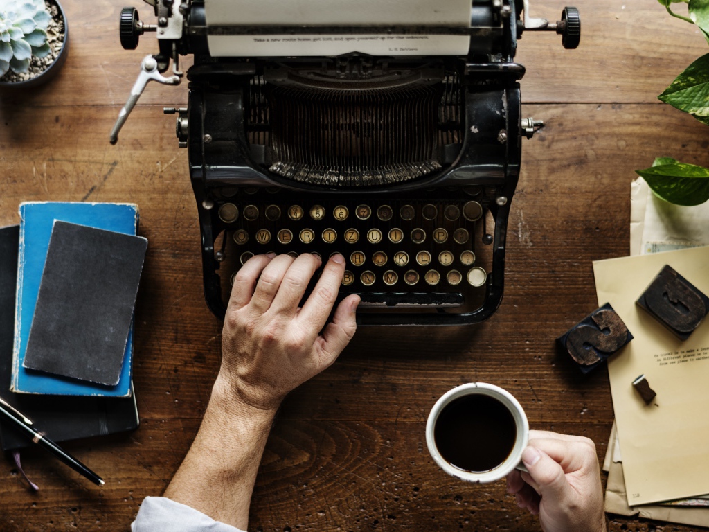 Мужчина с чашкой кофе в руке печатает на старой печатной машинке 