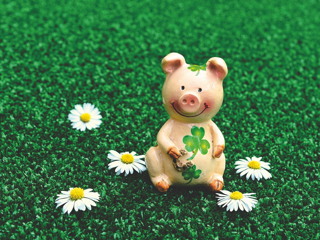 Статуэтка поросенка на зеленой траве с ромашками
