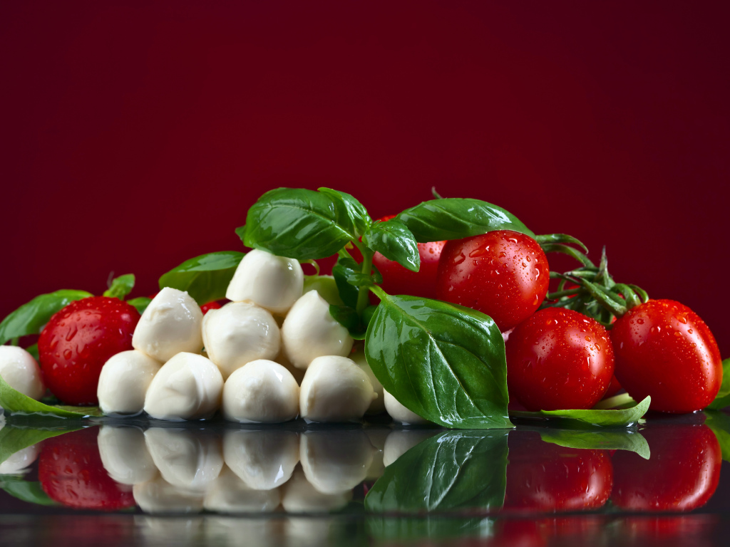 Сыр на столе с зеленью базилика и красными помидорами