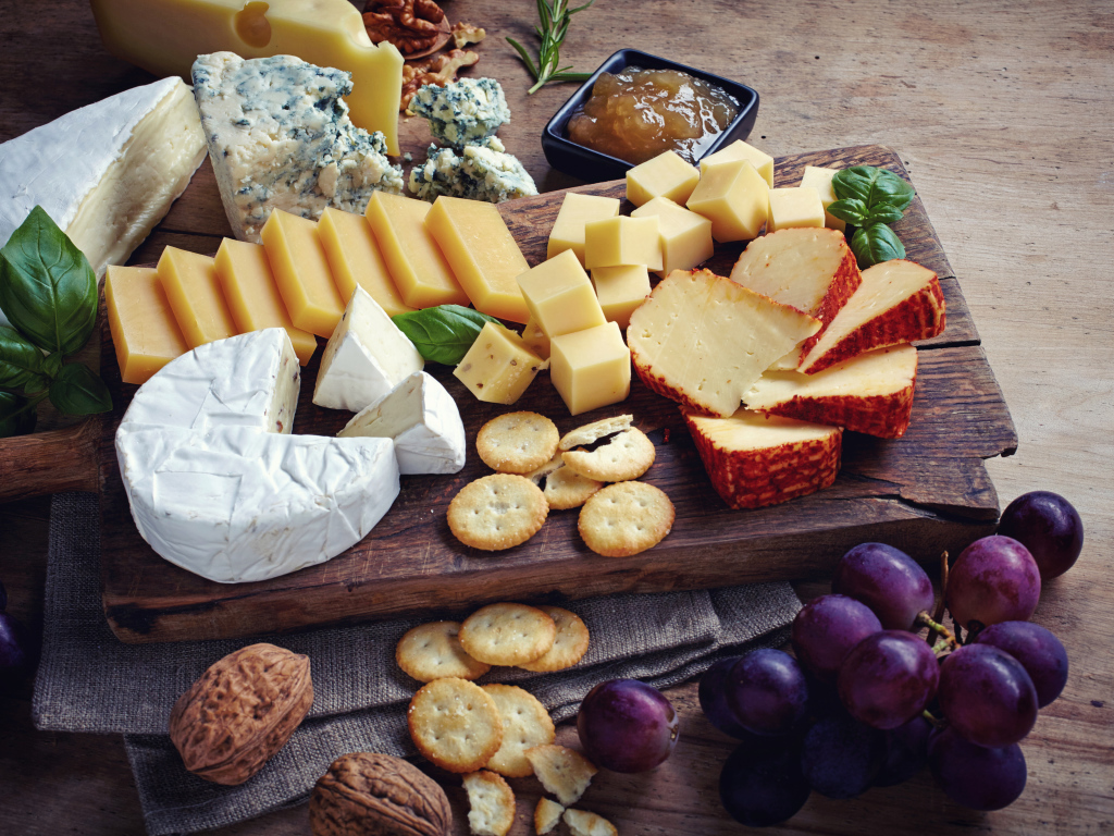 Сырная нарезка на разделочной доске на столе с виноградом и крекерами