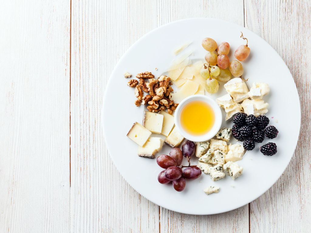 Куски сыра на тарелке с орехами, виноградом, медом и ягодами ежевики