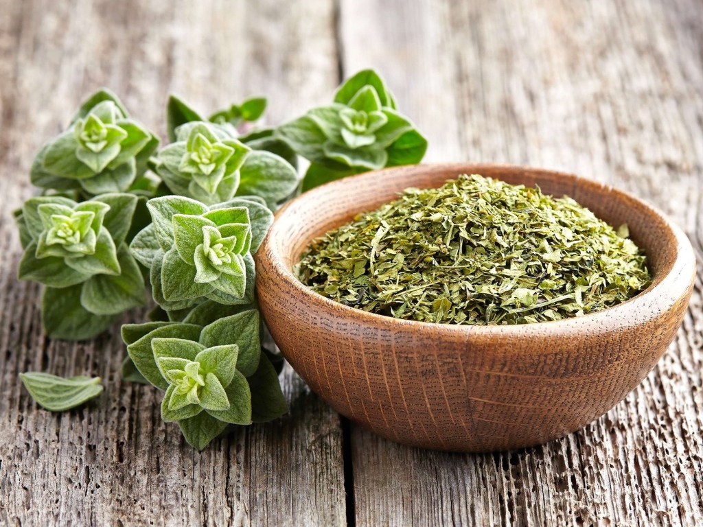 Сухая трава орегано в деревянной миске на столе 