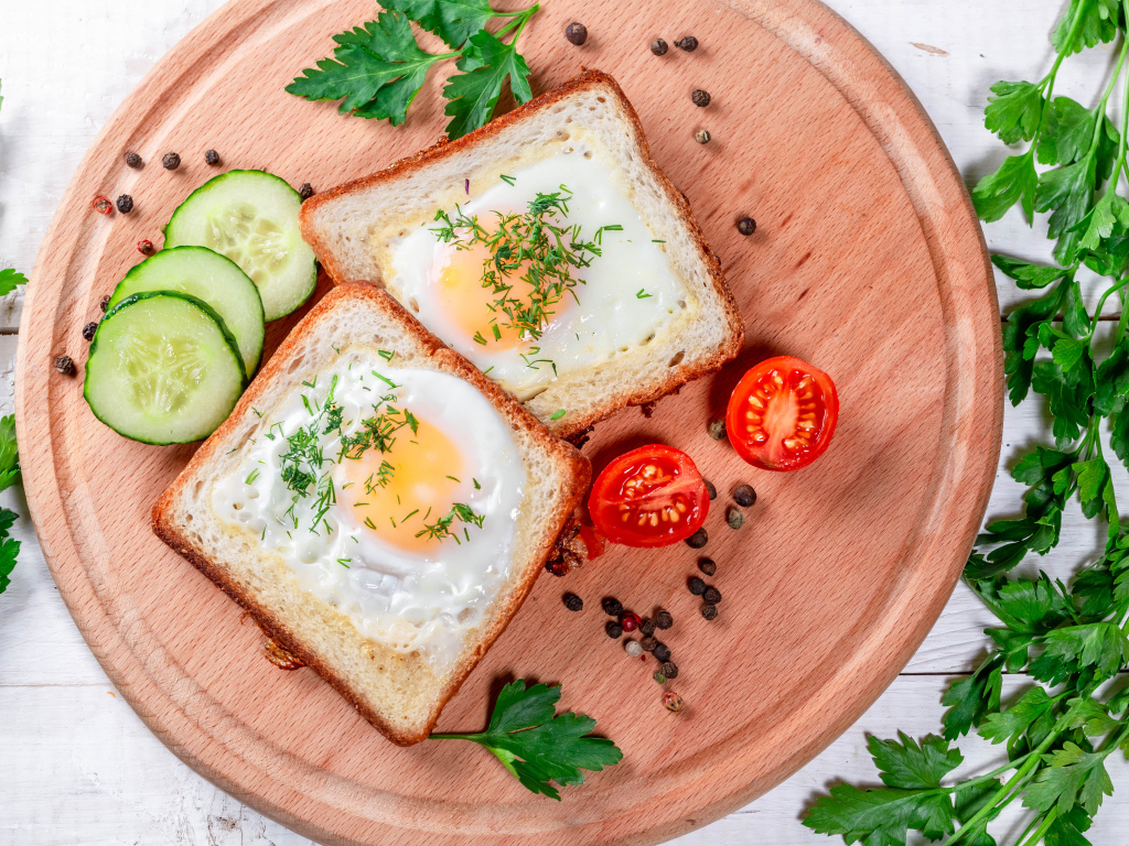 Яичница в хлебе на доске с помидорами, огурцами и петрушкой