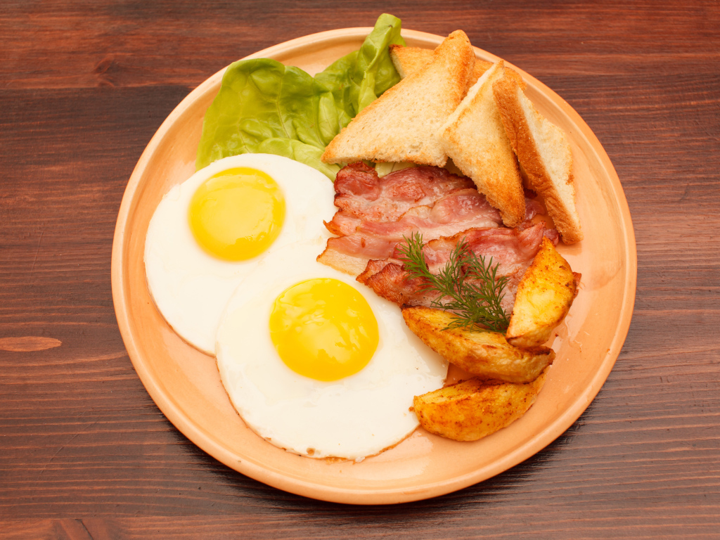 Яичница с беконом, картофелем фри и гренками на столе 