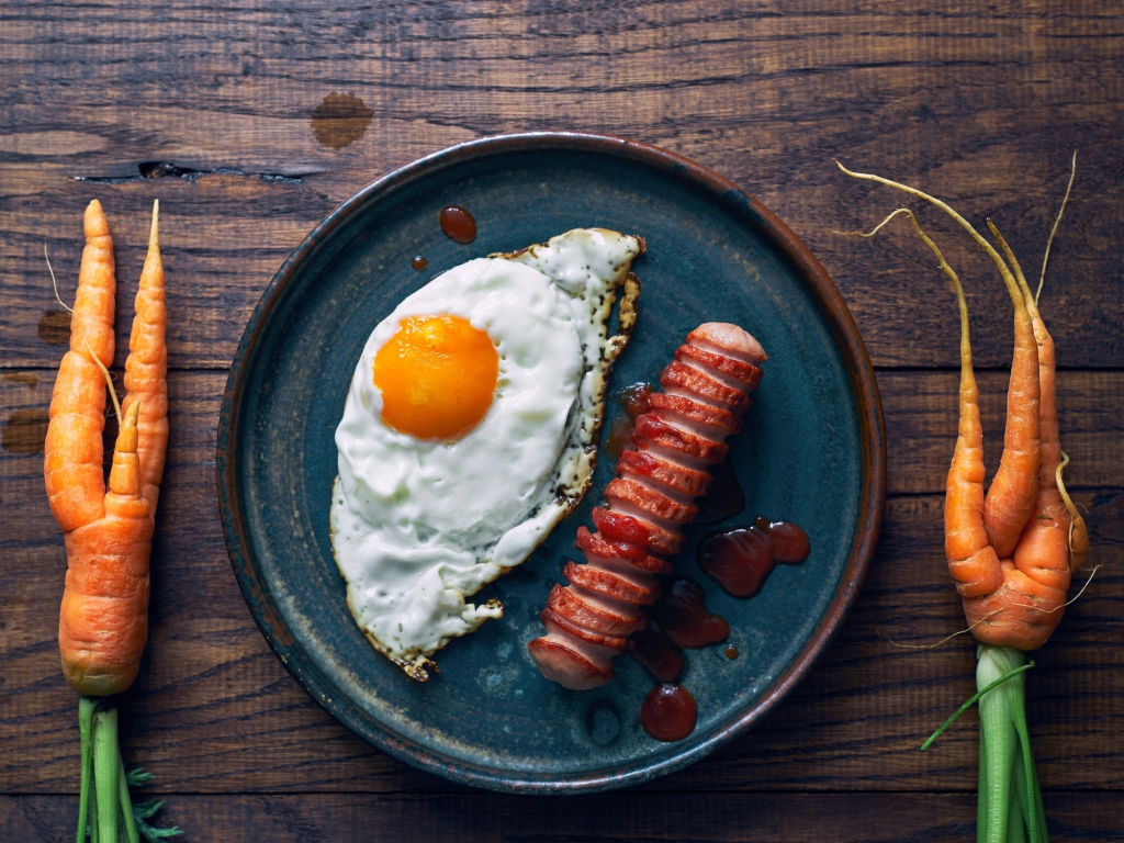 Яичница с сосиской на столе с морковью 
