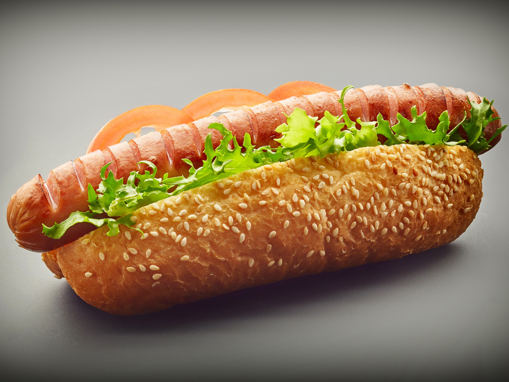 Хотдог с сосиской гриль и листьями салата на сером фоне