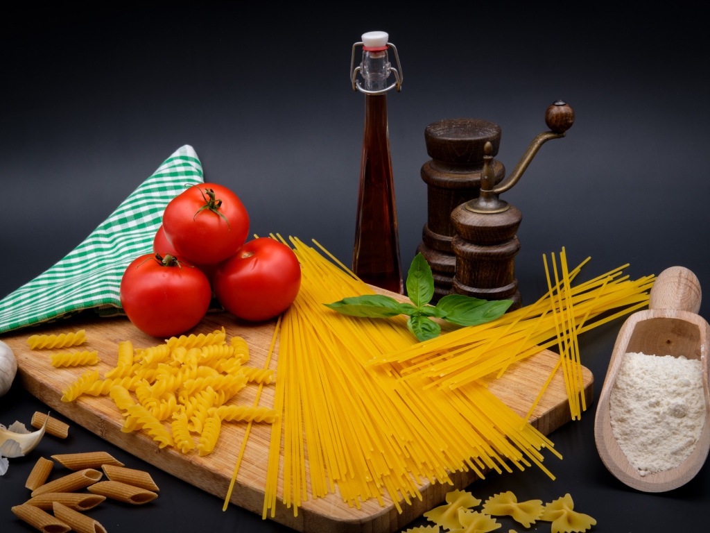 Макаронные изделия на столе с мукой, помидорами и специями