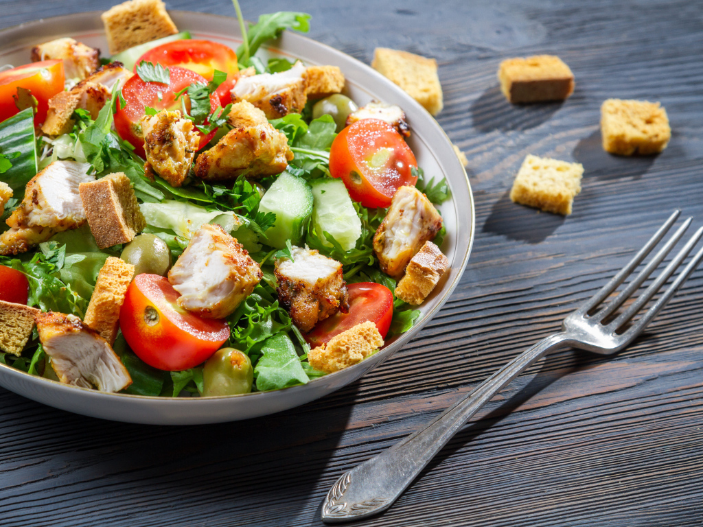 Салат с овощами, сухариками и курицей и на столе с вилкой