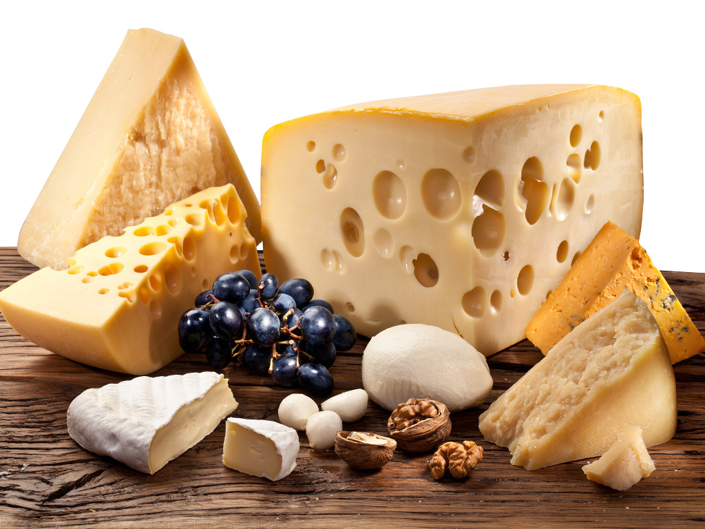 Куски сыра на деревянном столе с виноградом и грецким орехом