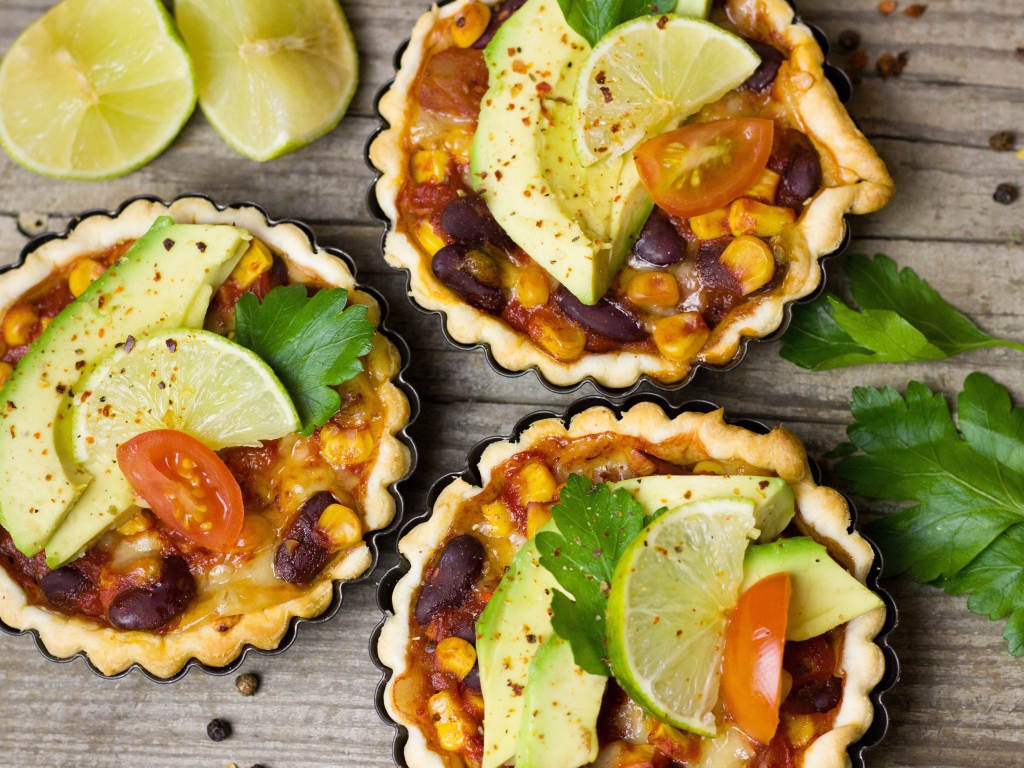 Тарталетки с блюдом, кусочками авокадо и лайма на столе