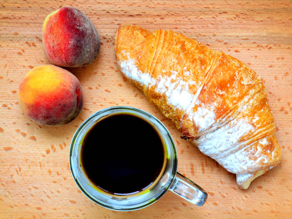 Два персика на столе с кофе и круассаном