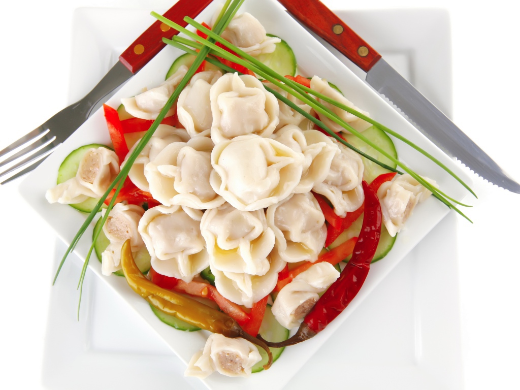Белая тарелка с пельменями, красным перцем и огурцами