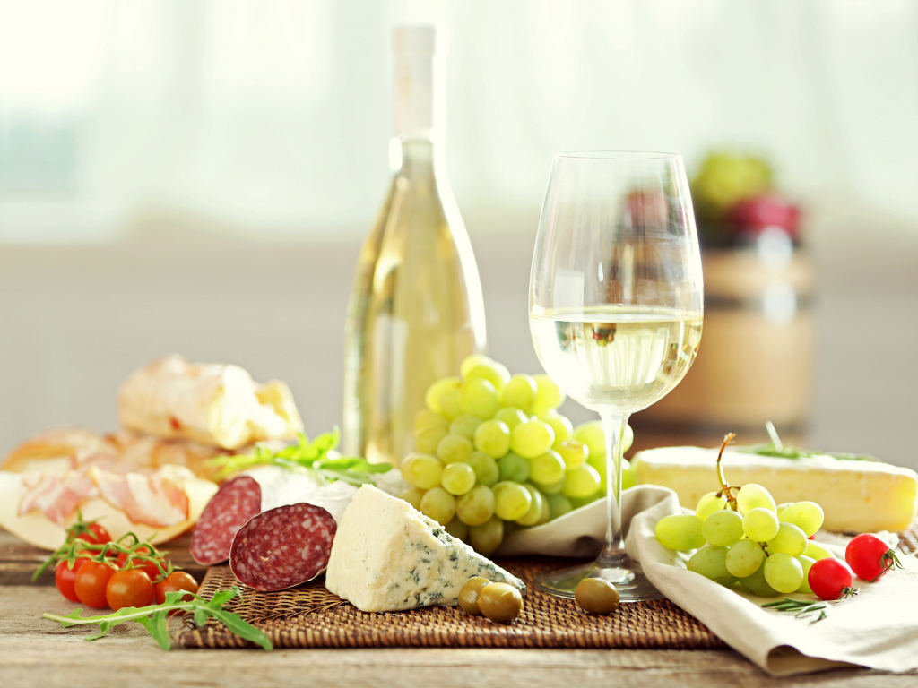 Белое вино на столе с сыром, колбасой и виноградом