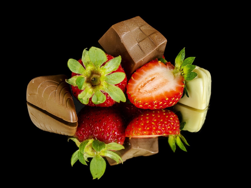 Красная свежая клубника с шоколадными конфетами на черном фоне