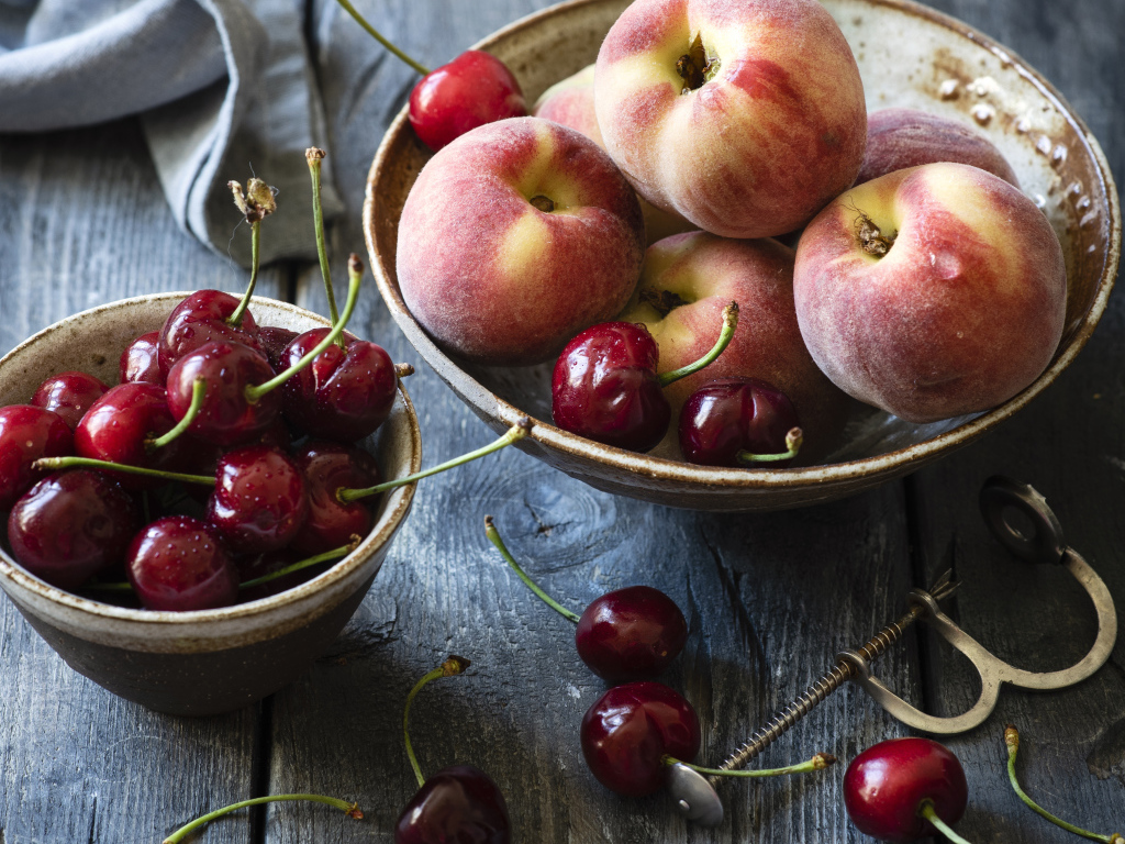 Спелые персики в миске на столе с черешней
