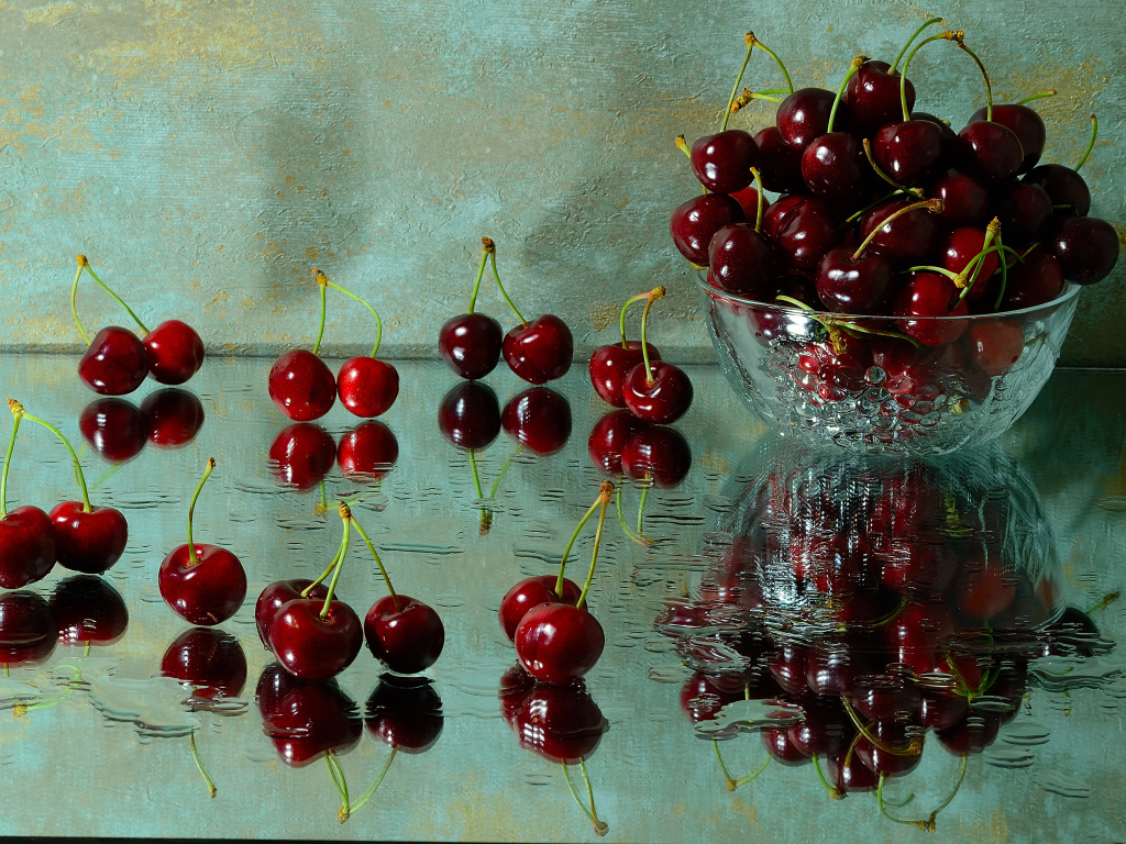 Спелые красные черешни отражаются в поверхности стола