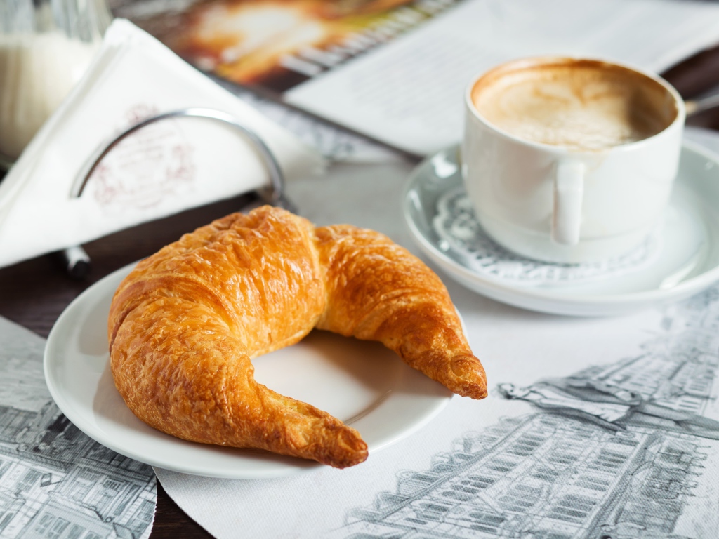 Круассан на белой тарелке с чашкой капучино 